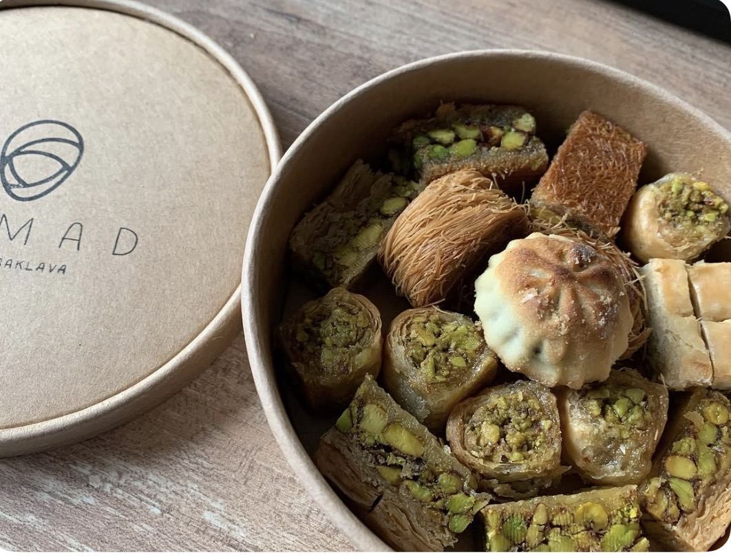Runde Pappbox mit Nomad-Baklava-Logo, gefüllt mit gemischtem Gebäck
