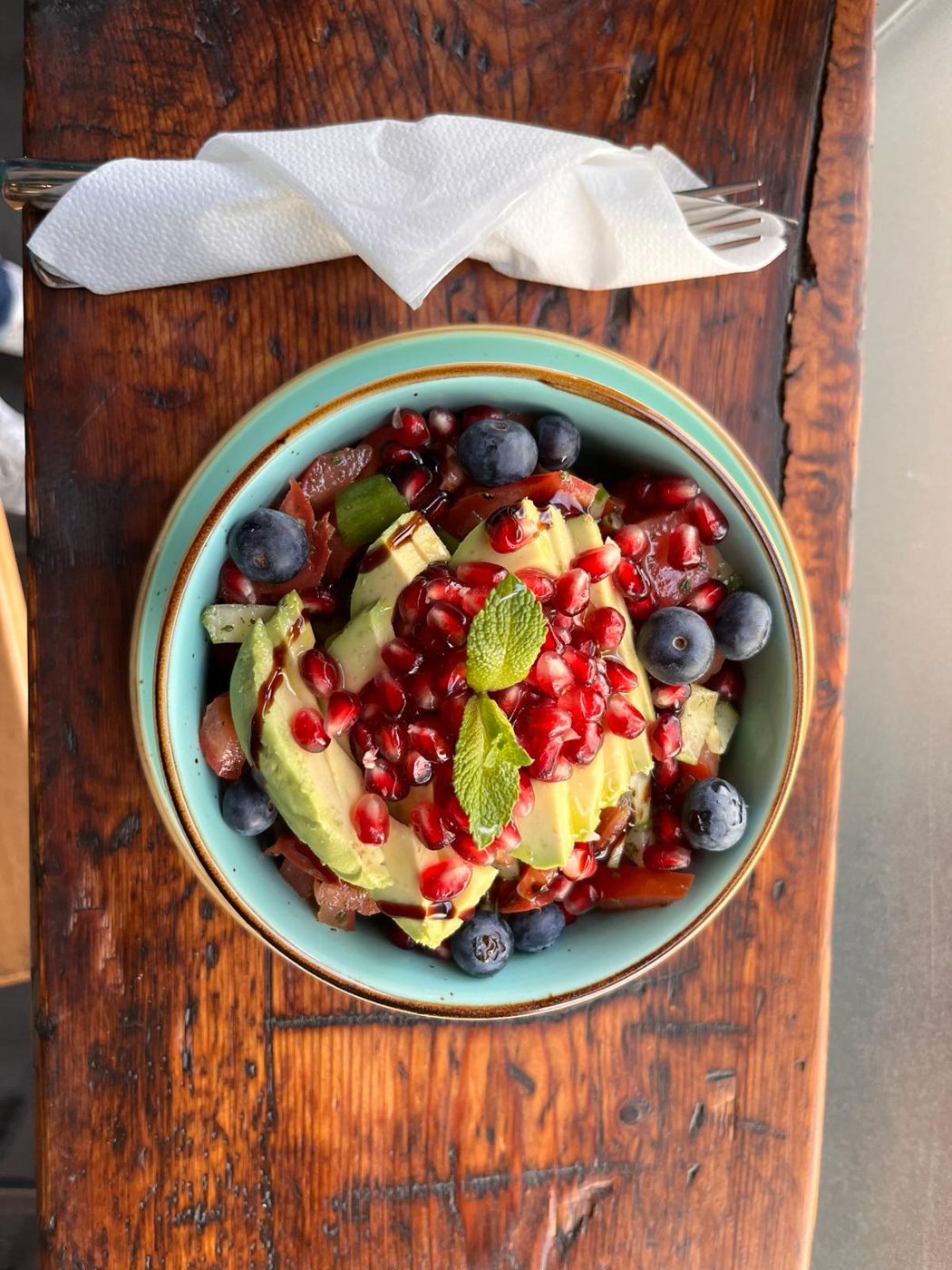Türkisfarbene Schale mit Avocado, Granatapfelkernen, Blaubeeren, Tomate, Gurke und Minze auf altem Holz