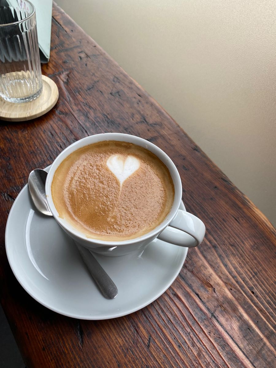 Cappuccino mit Herz auf der alten Holztheke am Fenster, daneben ein Glas Wasser