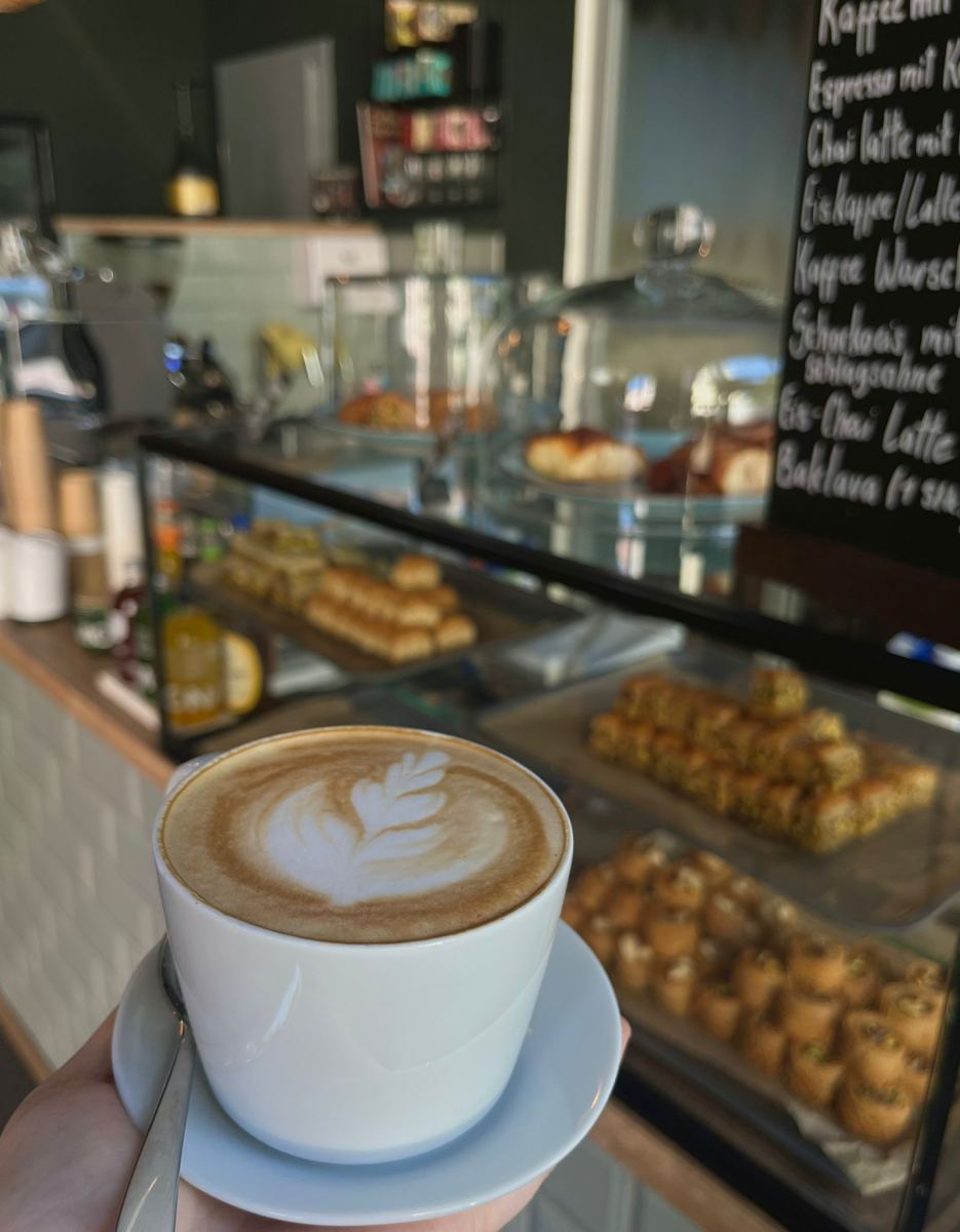 Cappuccino vor der Vitrine mit Baklava und der Kreidetafel an der Theke