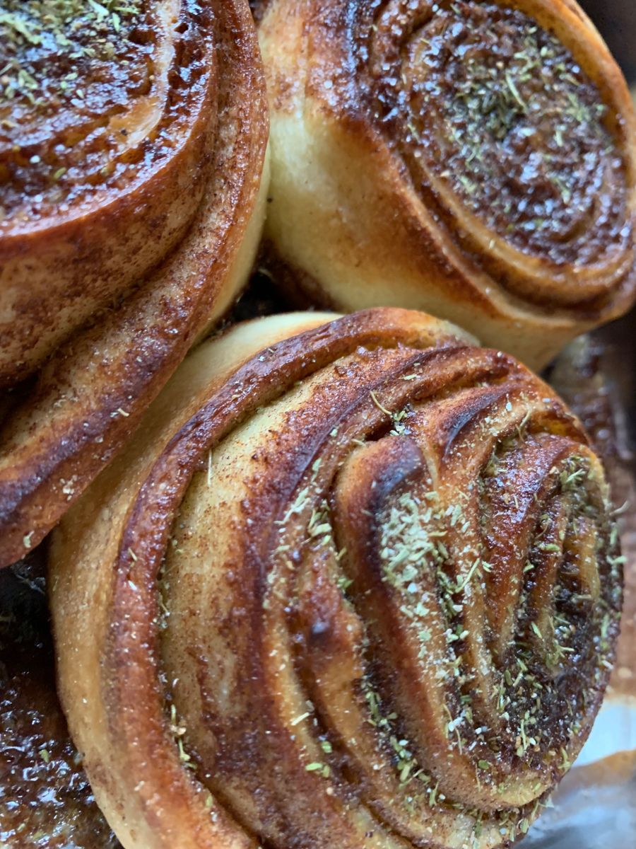 Nahaufnahme frisch gebackener Zimtschnecken mit karamellisiertem Rand, Zucker und grünen Gewürzflocken